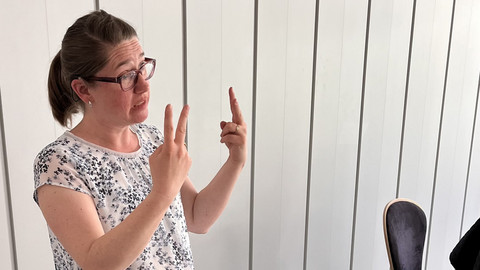 Frau Wegerhoff hat eine weiße Bluse an und gebärdet. 