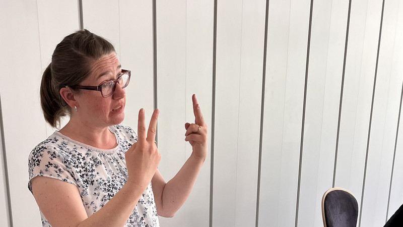 Frau Wegerhoff hat eine weiße Bluse an und gebärdet. 