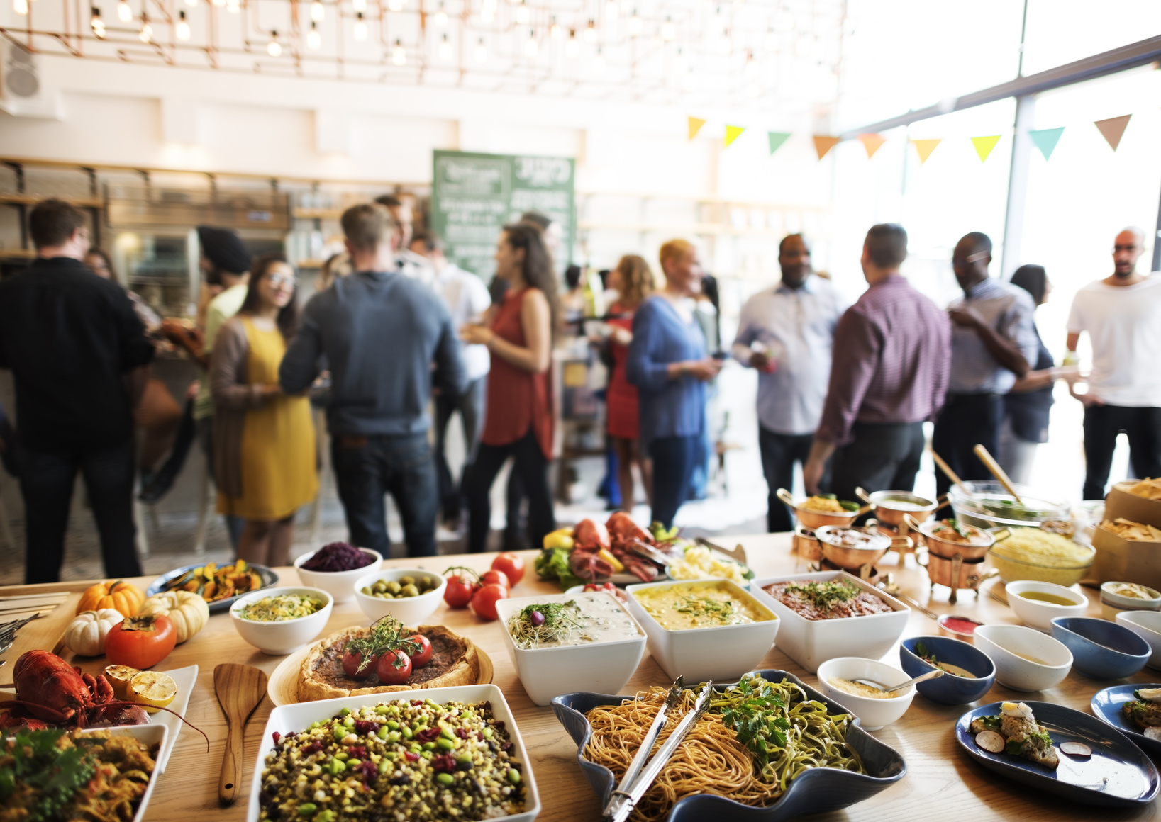 Im Vordergrund ist ein Buffet zu sehen. Im HIntergrund stehen Menschen