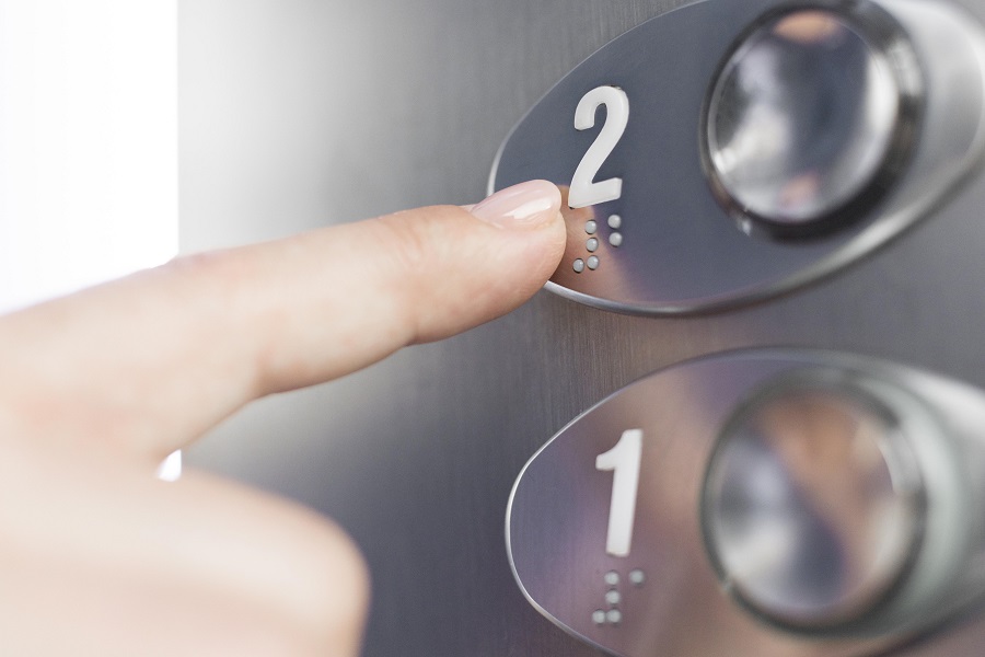 Zeigefinger drückt auf Fahrstuhlknopf mit Brailleschrift.