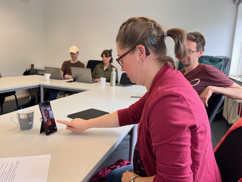 Frau Wegerhoff tippt mit dem Finger auf dem Smartphone am Tisch. 