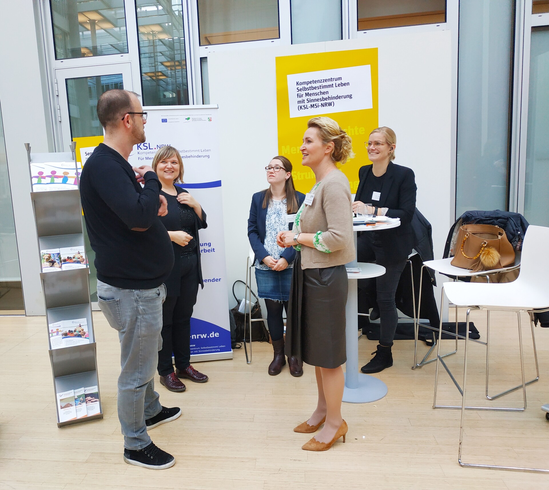 Es stehen fünf Personen am Messestand. Links steht ein Mann, hinten am Messestand sind Anna Cebulla, Melanie Wegerhoff und Kristin Reker. Vorne rechts steht Frau Janaszek und spricht mit dem Mann.